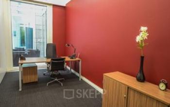 Modern Zurich Enge office space rental at Dreikönigstraße 31A featuring a vibrant red wall, furnished with a desk, chair, and wooden cabinet.